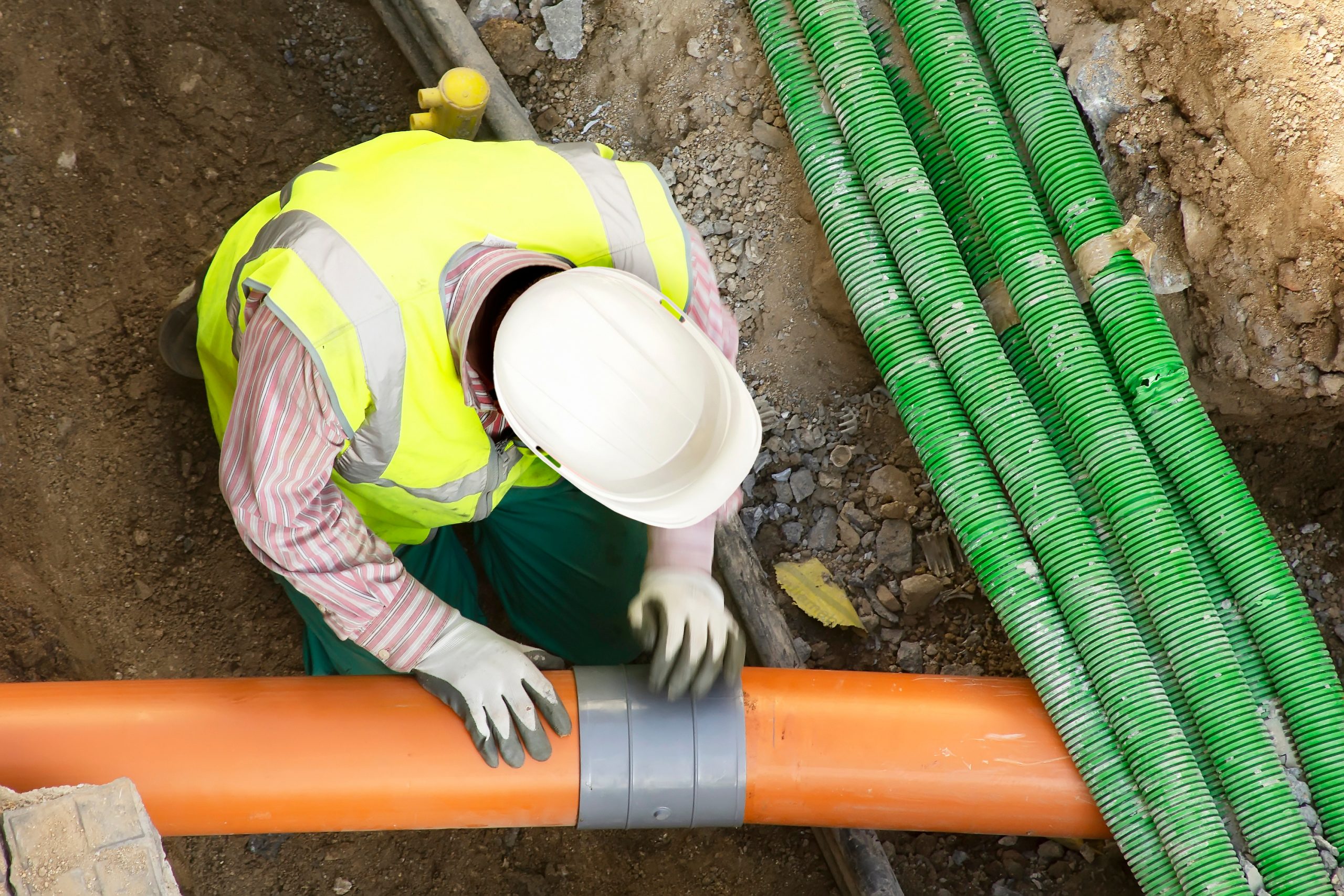 The Standardization Advantage: How Consistent Enclosures Improve System Performance for Utility Co‑Ops 2 worker installing hdpe corrugated electric and sewer pipes at the construction site on street city